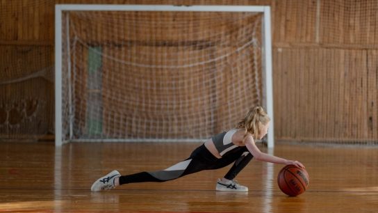 A young girl stretching with a basketball in an indoor sports hall.